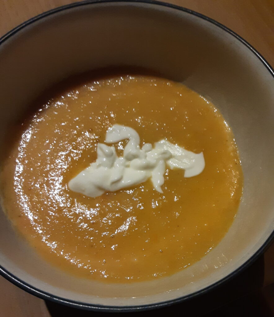 A bowl of soup that looks a light orange colour with dollops of white natural yoghurt in the middle.