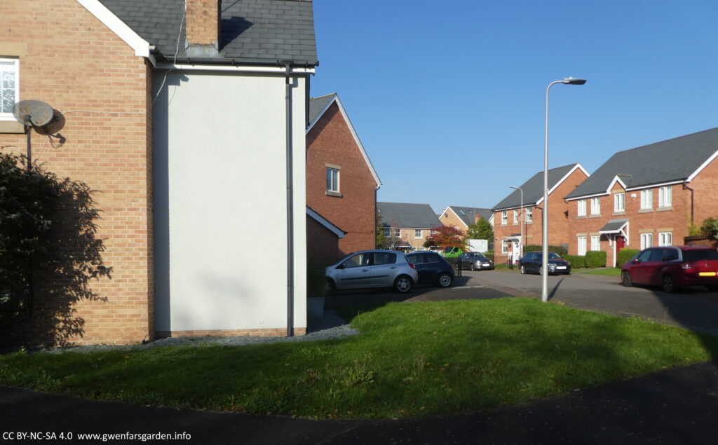 A view of the front garden from the side. You can see the lawn, though it looks smaller than it is in reality, approx 7m x 12m. You can also see the street, other cars and houses.