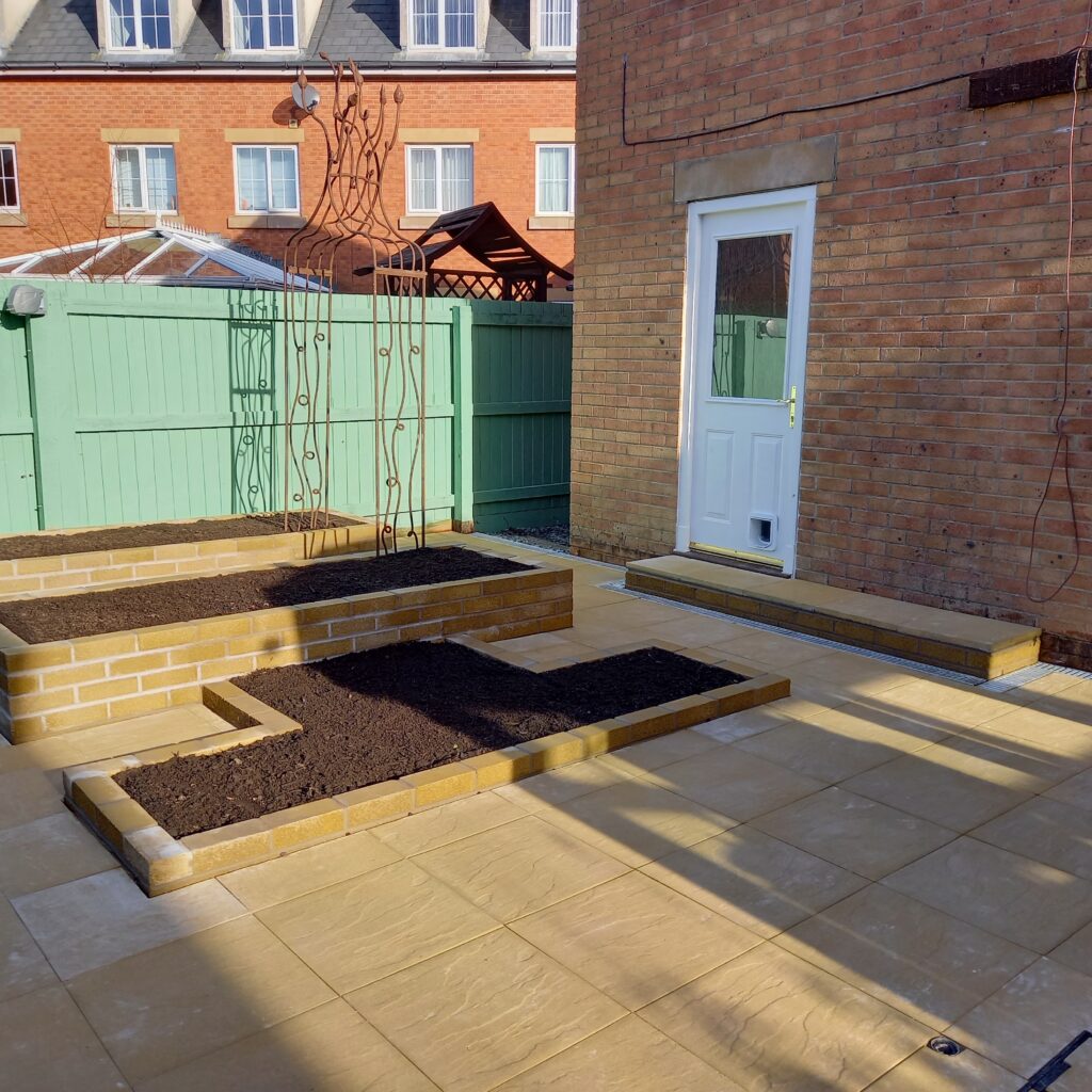 A section of the back garden that has been completed by the landscapers. You can see the layout with two raised beds and one lower ornamental bed, paving, and rusted steel arch. This backs on to the back of the house.