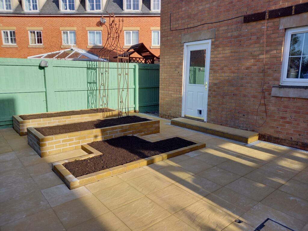 A section of the back garden that has been completed by the landscapers. You can see the layout with two raised beds and one lower ornamental bed, paving, and rusted steel arch. This backs on to the back of the house.