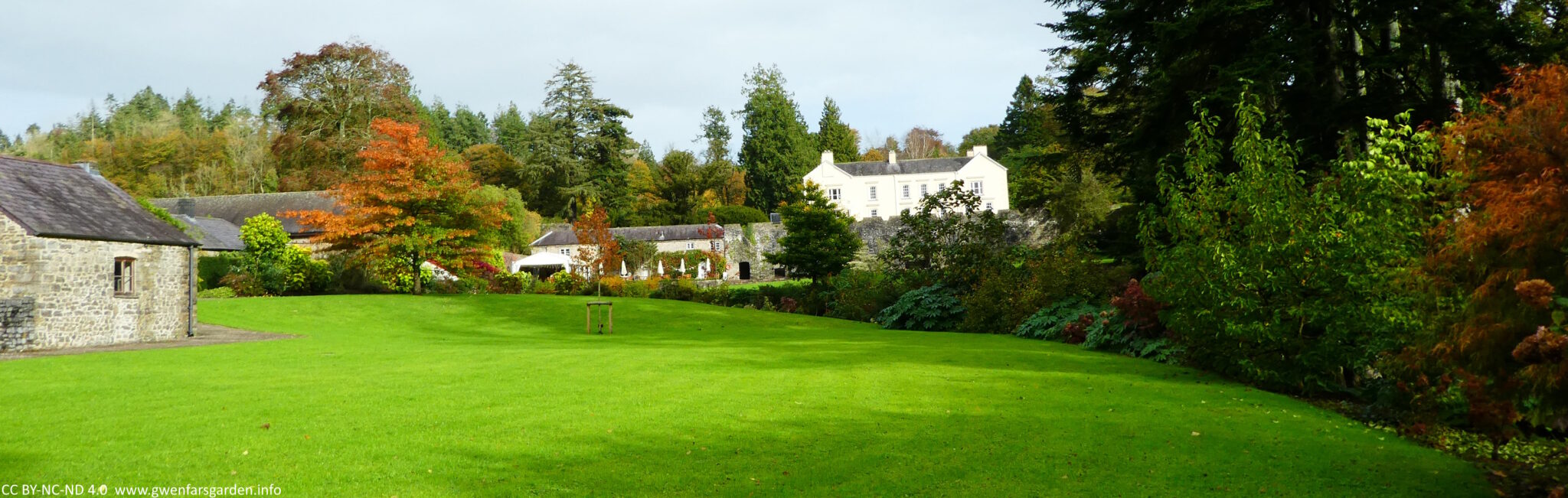 A landscape photo of a large area of lawn with lots of trees in different shades of autumn colours.